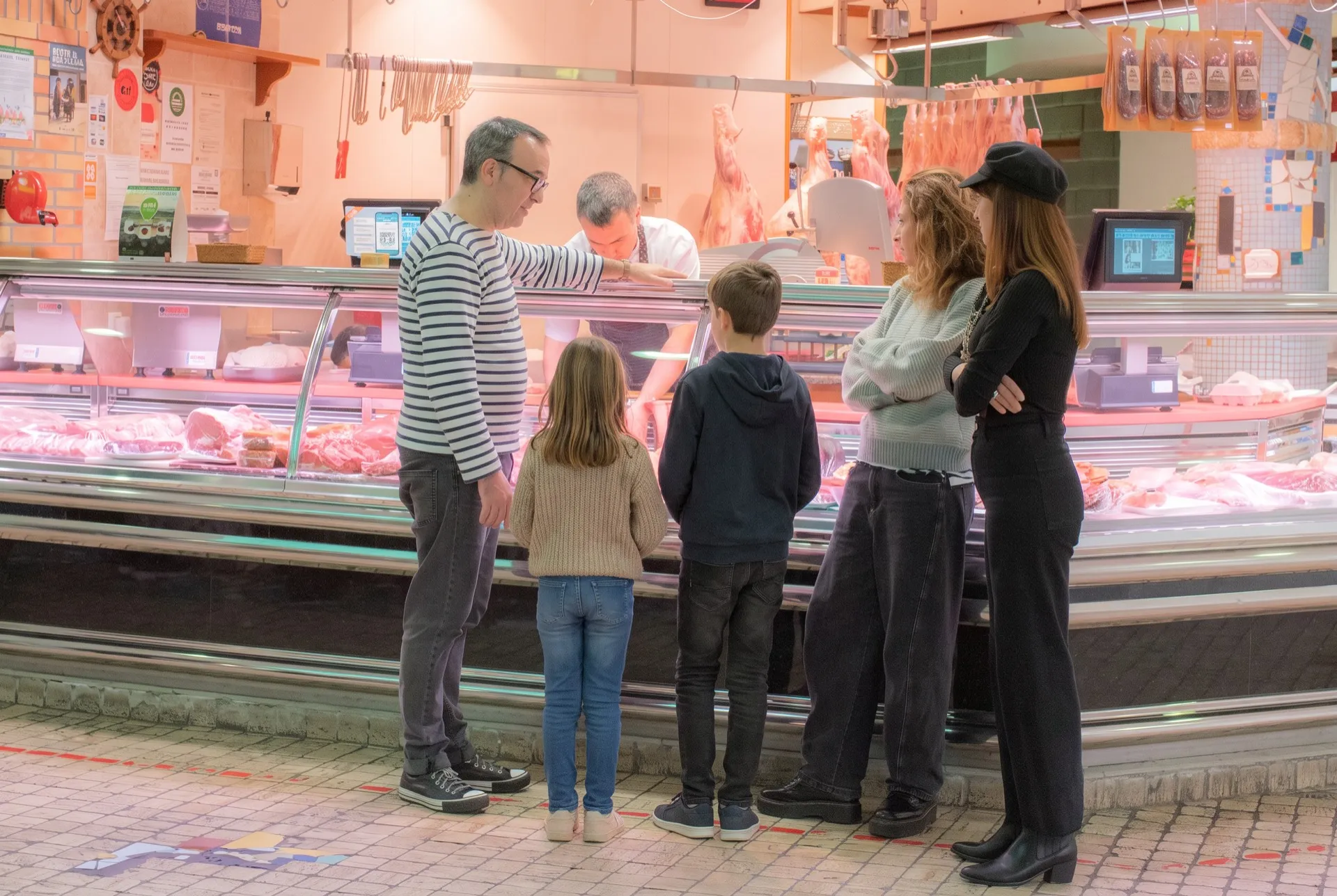 Chef Ben guiding a family through La Bretxa market, pointing out ingredients at the butcher's counter